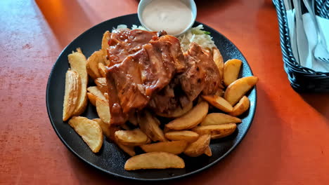 vista hacia adelante de la comida en un plato negro, costillas cocidas con patatas de cuña a un lado