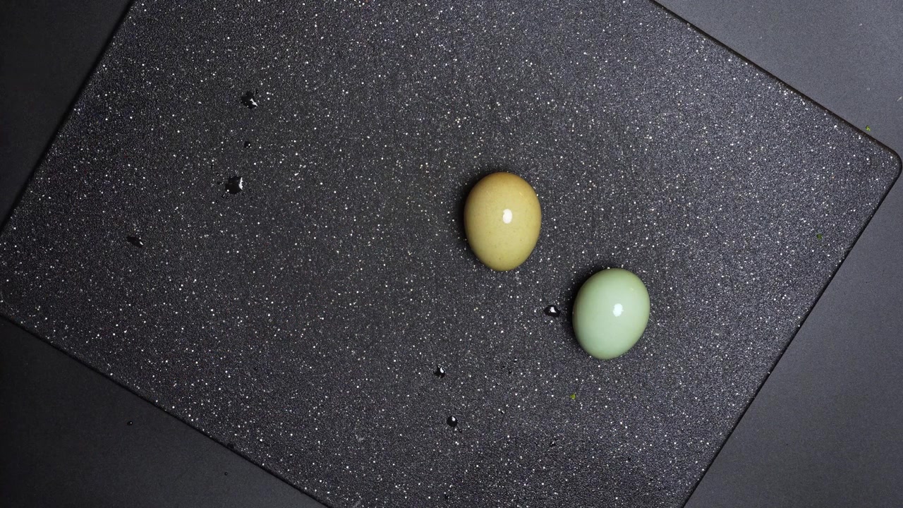Person scooping soft boiled egg from water with spoon. Top view of a hand using a black spoon to remove a light-colored egg from a bowl of water.