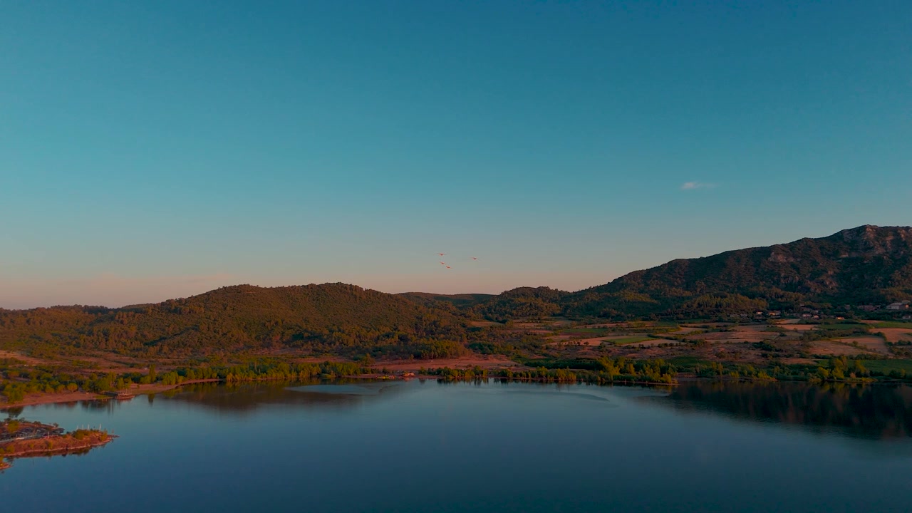 Vista aerea di un lago calmo e colline boscose sotto un cielo azzurro limpido all'ora d'oro.