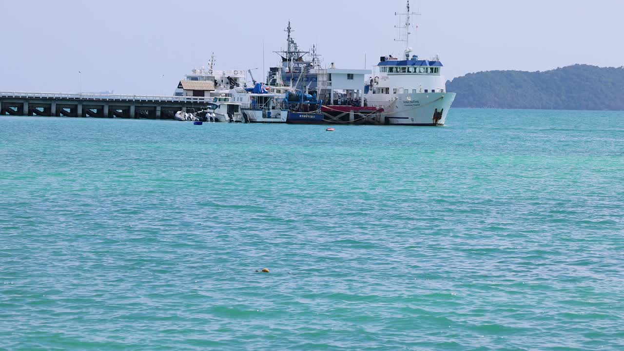 A marine research vessel approaches and docks at a pier in Phuket, Thailand. Calm turquoise waters and clear skies enhance the serene atmosphere
