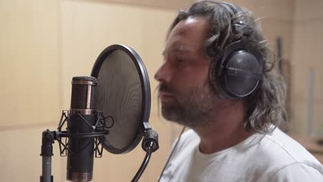 grabando voces en el micrófono del condensador, chico divertido de pelo largo, vista de cerca