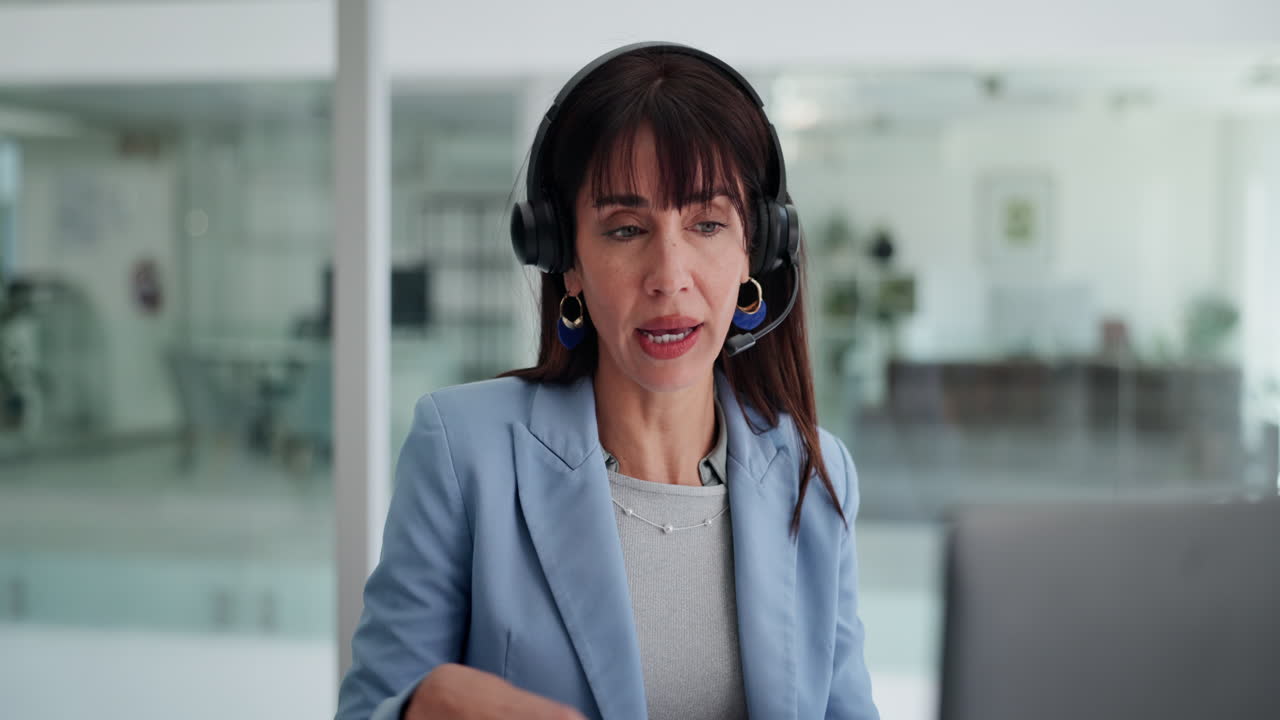 Mujer profesional con auriculares hablando durante una videollamada en la oficina.