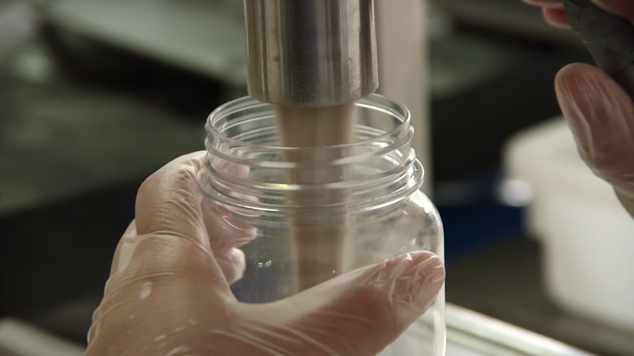 mano sosteniendo una botella llena de condimentos por una máquina en una fábrica