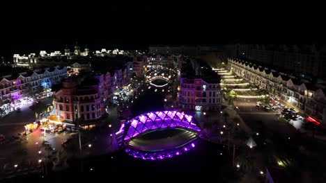 nighttime aerial video showcases a brightly illuminated urban waterfront in phu quoc featuring european-style buildings along a canal crossed by illuminated pedestrian bridges and lively evening walks