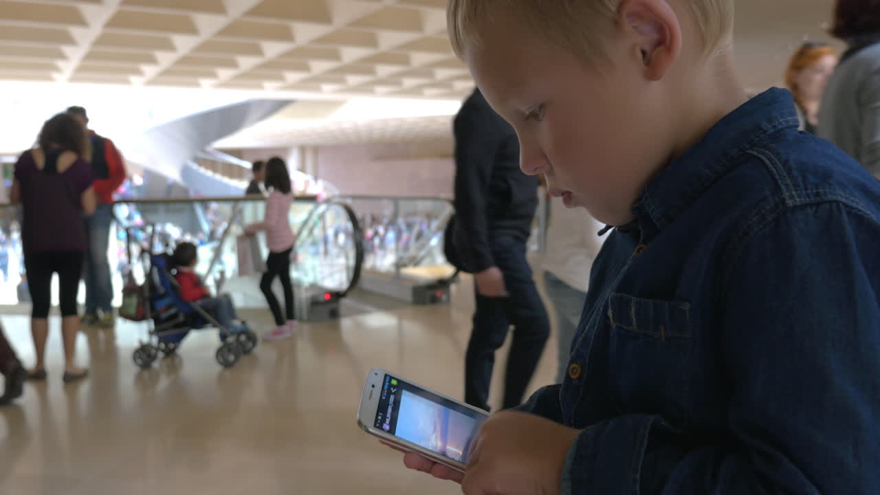 niño usando teléfono inteligente en un centro comercial ocupado