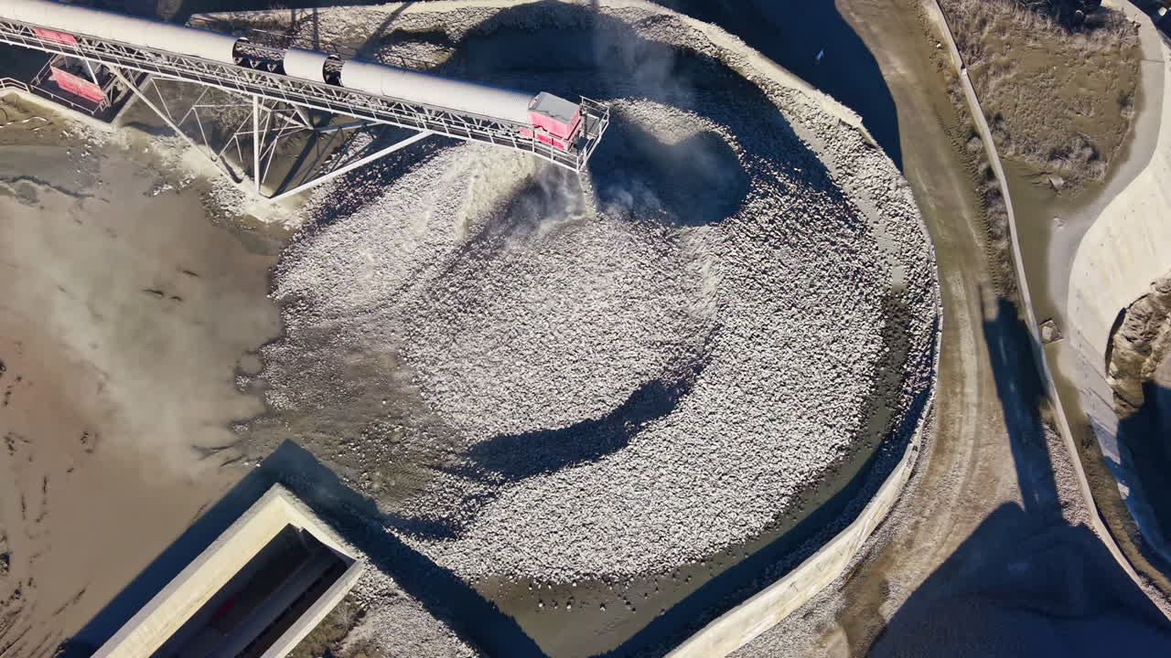 Un incredibile treno scarica un enorme carico di ghiaia nel cantiere edile, circondato da macchinari e terra texturizzata sotto un cielo azzurro.
