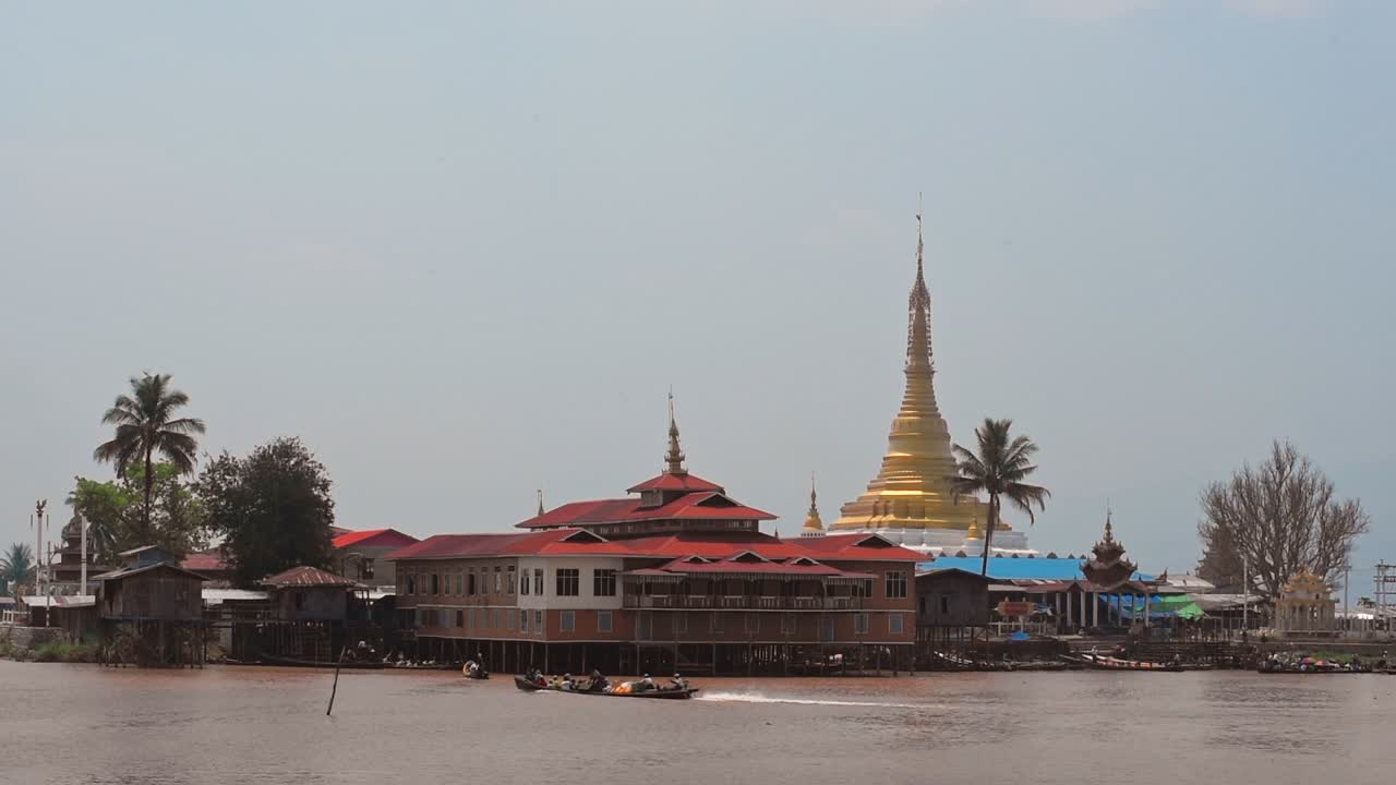 Traditional buildings near the shoreline of Inle Lake, Myanmar, with canoe passing by