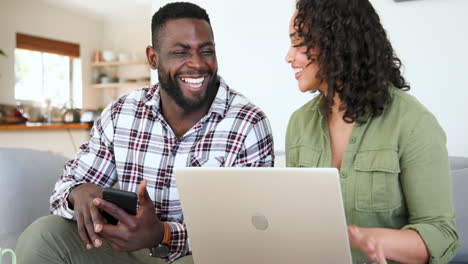 happy multiracial couple using smartphone and laptop at home, enjoying time together