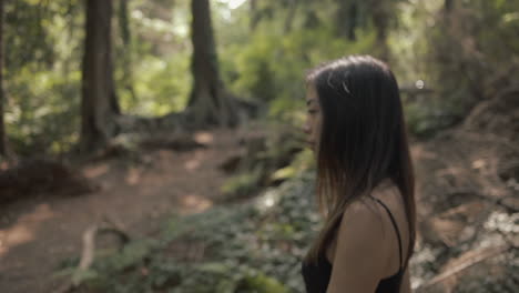 medium closeup profile shot of asian woman in black exploring sunny forest, slowmo