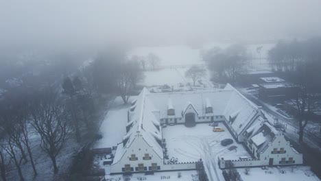 drone flying away from beautiful snow covered old farm in rural holland in winter