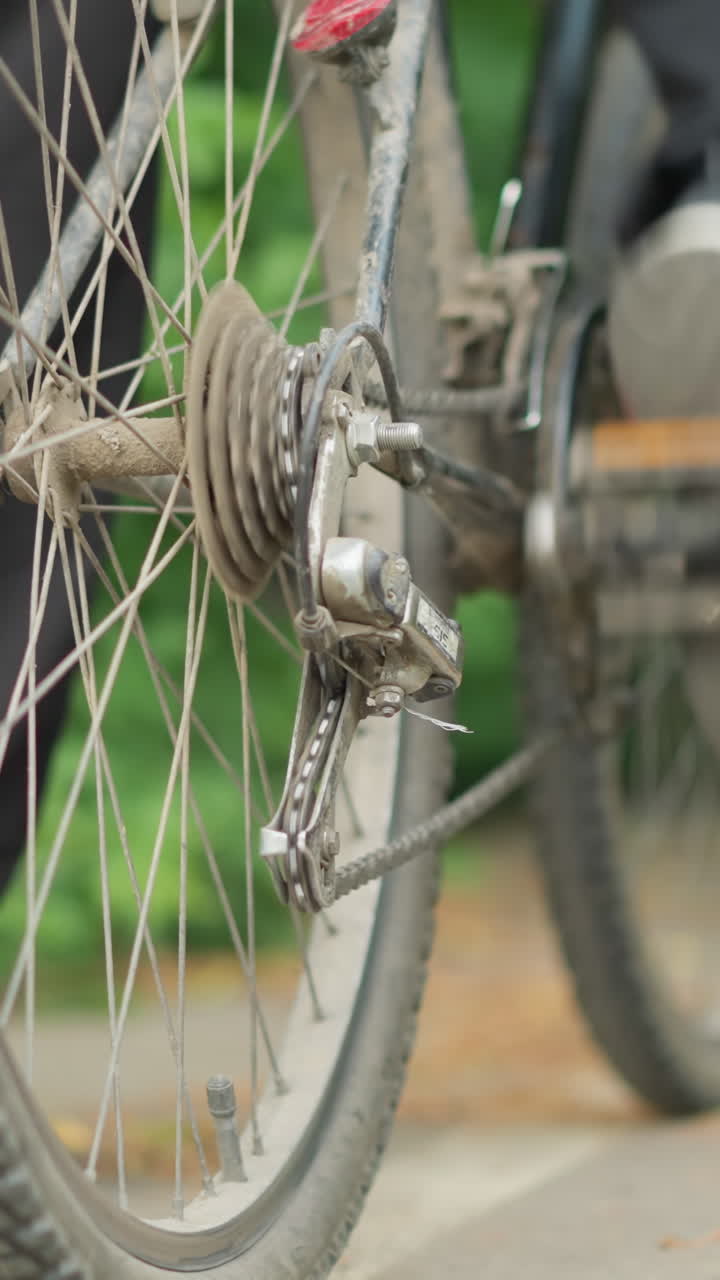 자전거의 페달을 뒤로 회전시키는 누군가의 클로즈업, 포장된 경로에 발을 고, 배경에는 흐릿한 초록색이 있습니다.