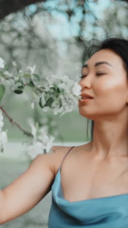 woman in blue dress smelling flowers