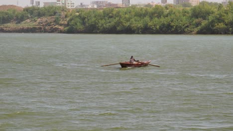 man rowing a small fishing boat across the nile river near khartoum, sudan
