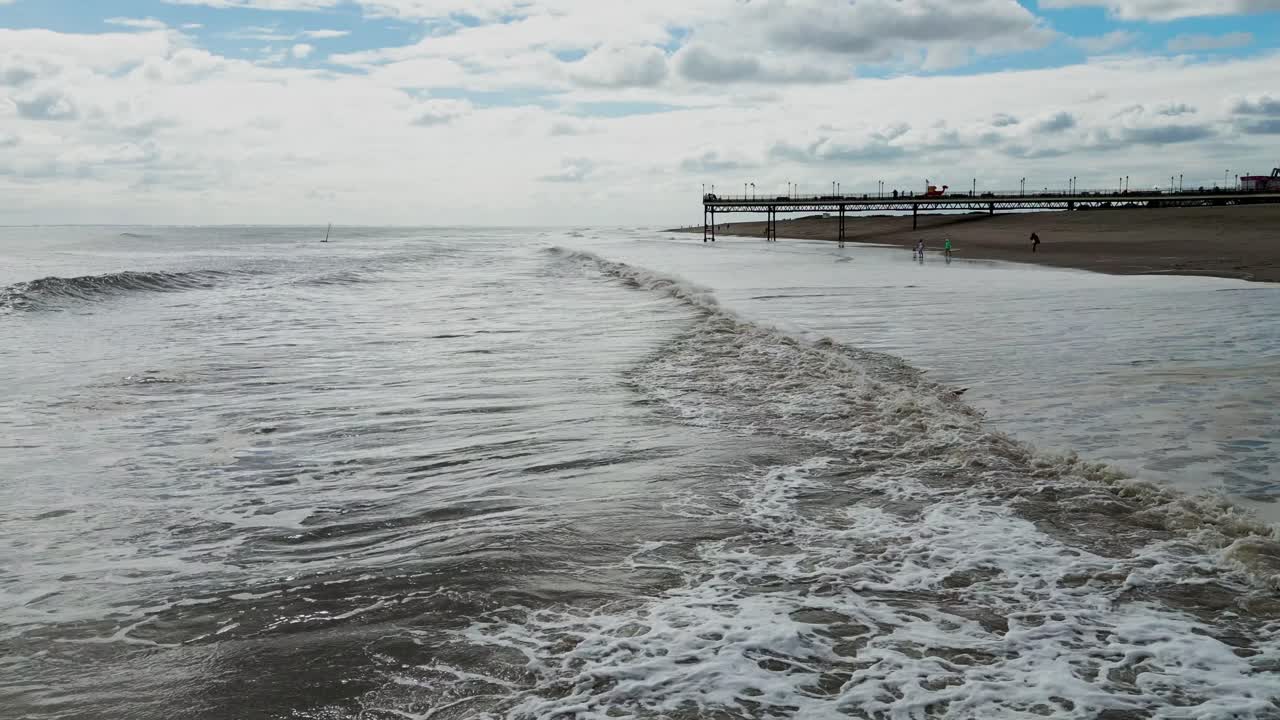 Typical English seaside tourist resort, shot using a drone, giving a high aerial viewpoint showing a wide expanse of sandy beach with a pier and crashing waves