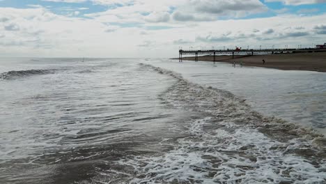 Typical-English-seaside-tourist-resort,-shot-using-a-drone,-giving-a-high-aerial-viewpoint-showing-a-wide-expanse-of-sandy-beach-with-a-pier-and-crashing-waves