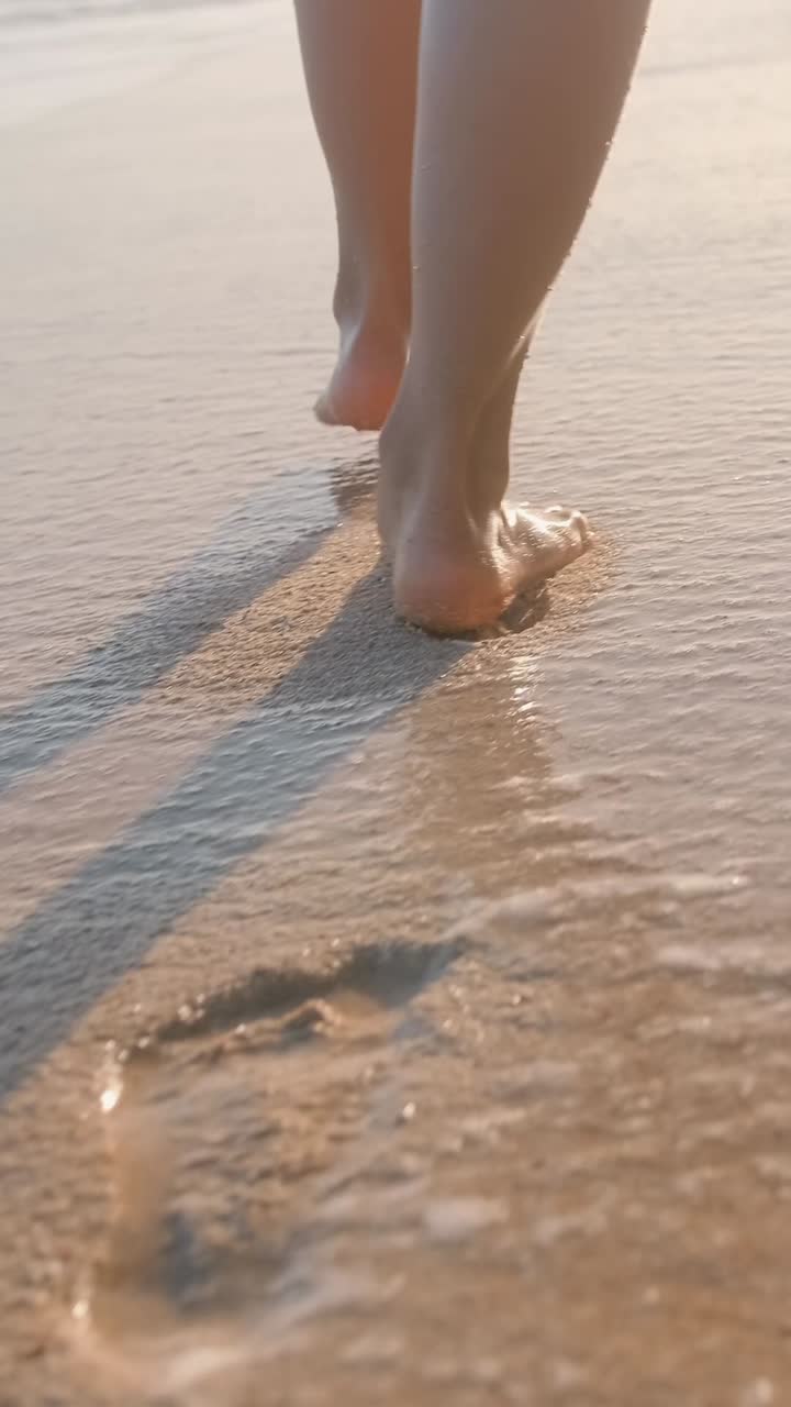 Legs of woman walking along sandy beach washed by foamy waves on southern island