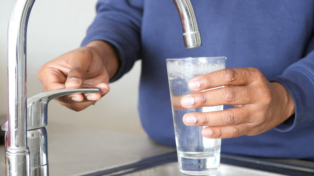 persona llenando un vaso con agua de un grifo de la cocina