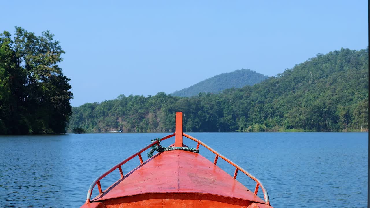 View from a boat's bow as it glides through a serene lake surrounded by lush greenery and distant hills.