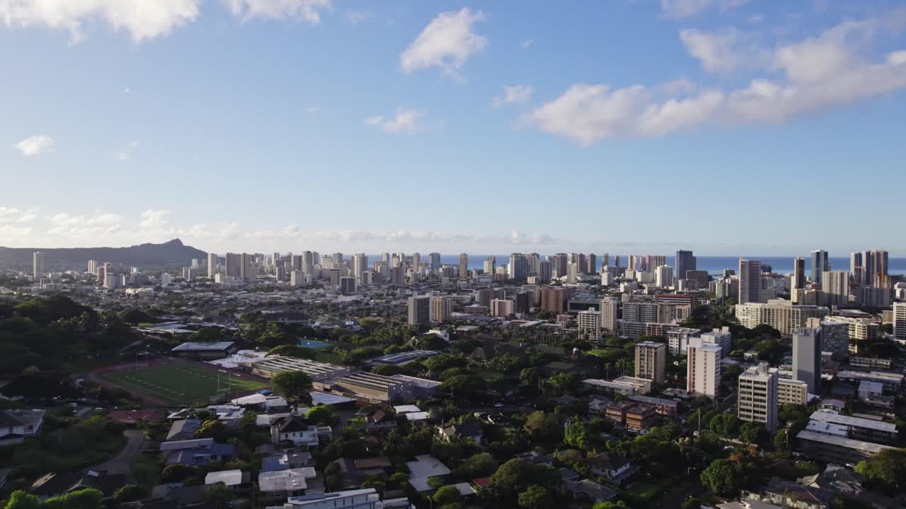 Ripresa drone con panoramica a destra della città di Honolulu, Hawaii, in un pomeriggio soleggiato con cielo azzurro, con alti edifici nel contesto urbano sullo sfondo dell'Oceano Pacifico