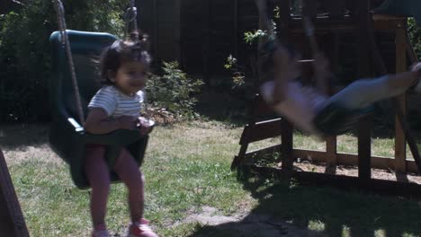 adorable baby and older sister on swing together in the garden