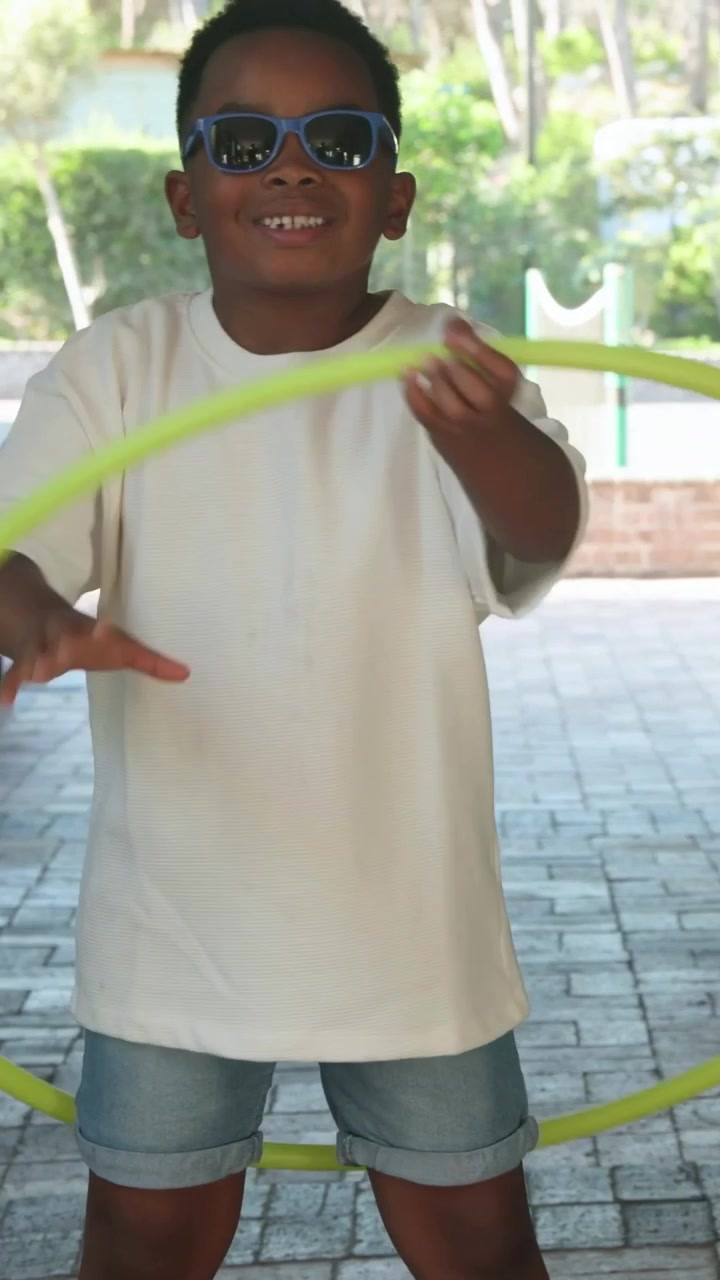 Vertical video: Picking neon hoop, youth practicing waist spinning under pavilion in white T-shirt