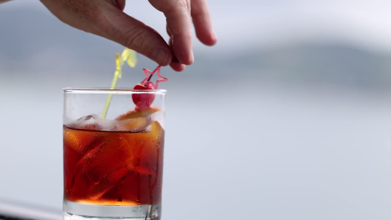 평온한 바다를 배경으로 장식된 지이로 네그로니 테일을 는 손은 휴식의 순간을 포착합니다.