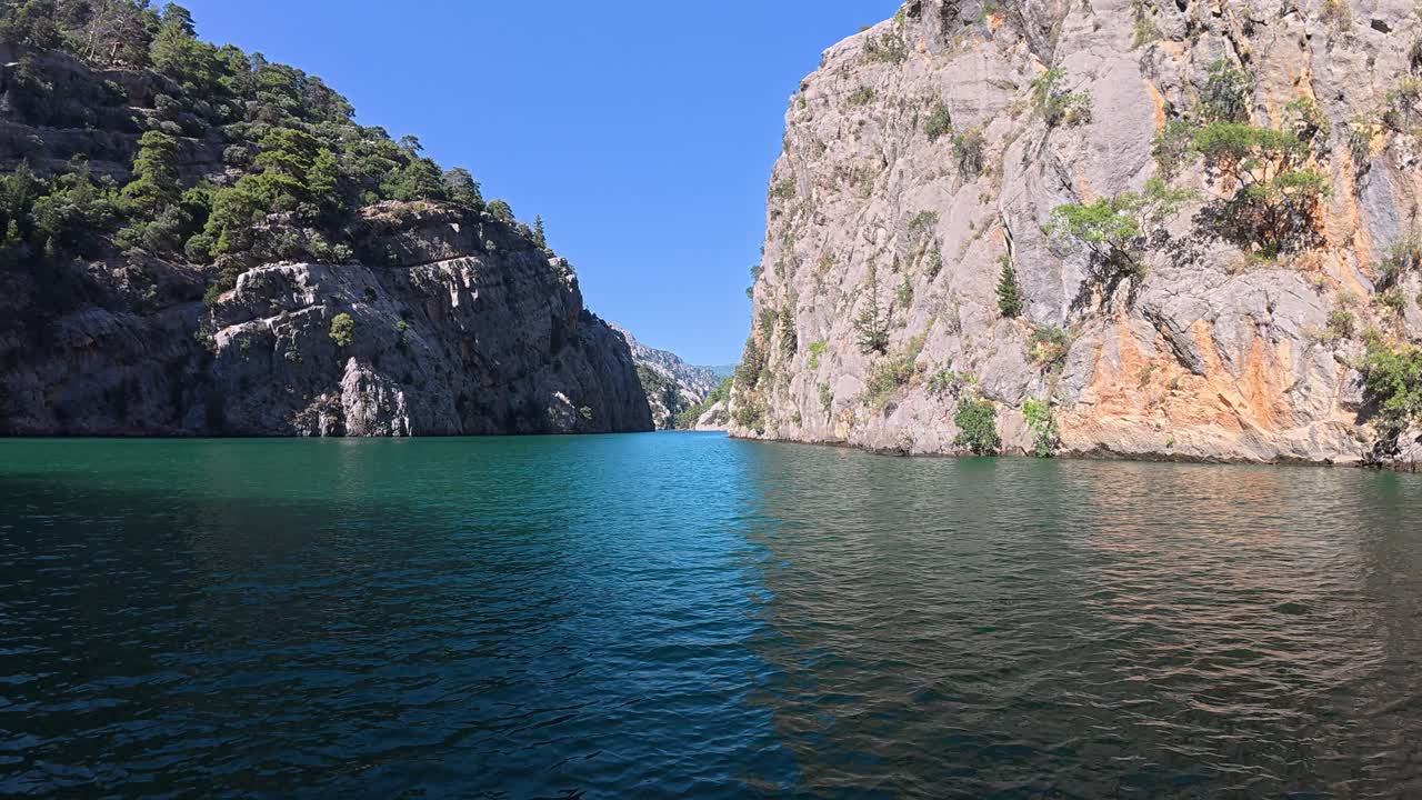 Slow scenic cruise through turquoise canyon waters in southern Turkey. Tall white cliffs reflect sunlight under clear blue sky