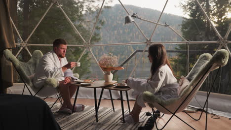 couple enjoying coffee and breakfast in a cozy dome tent with a stunning mountain view