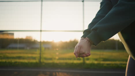 close-up hand view of someone in green hoodie hitting volleyball with sunlight glow effect around hand, open field and distant building in background during golden hour