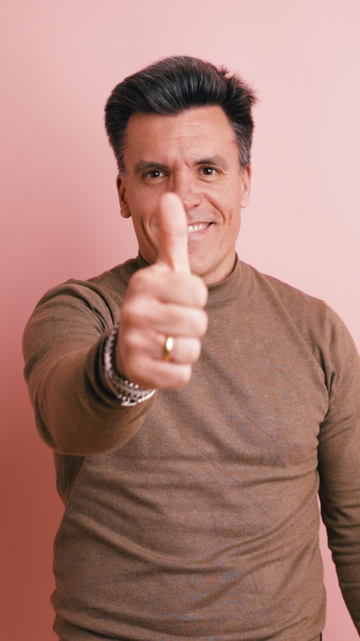 Uomo sorridente che fa il gesto del pollice in su su sfondo rosa