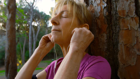 Mujer-Mayor-Apoyada-En-Un-árbol-Y-Escuchando-Música-4k