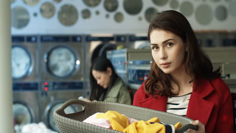 portrait shot of young pretty woman smiling to camera and holding basket with dirty clothes while standing in laundry service