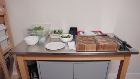 the camera tilts man down on a food prep table with organic healthy food modern vegetable bins plates cutting board knives plates and cooking accessories inside a professional chef home kitchen