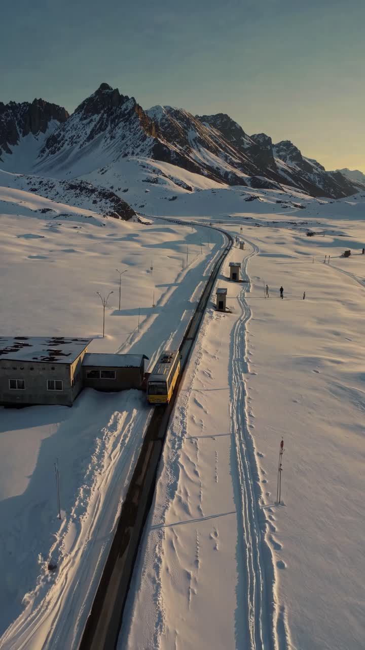 Aerial view of a train on a snowy landscape with mountains. The video captures the serene winter