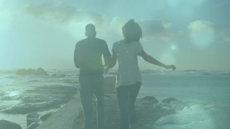 animation of spots of light over african american couple running on the rocks near the sea