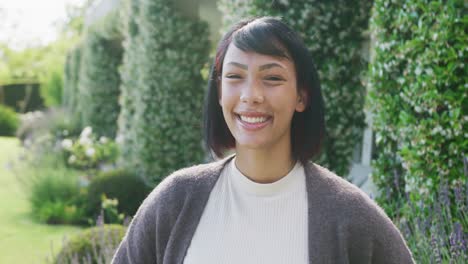 portrait of happy biracial teenager girl looking at camera and smiling in garden, in slow motion