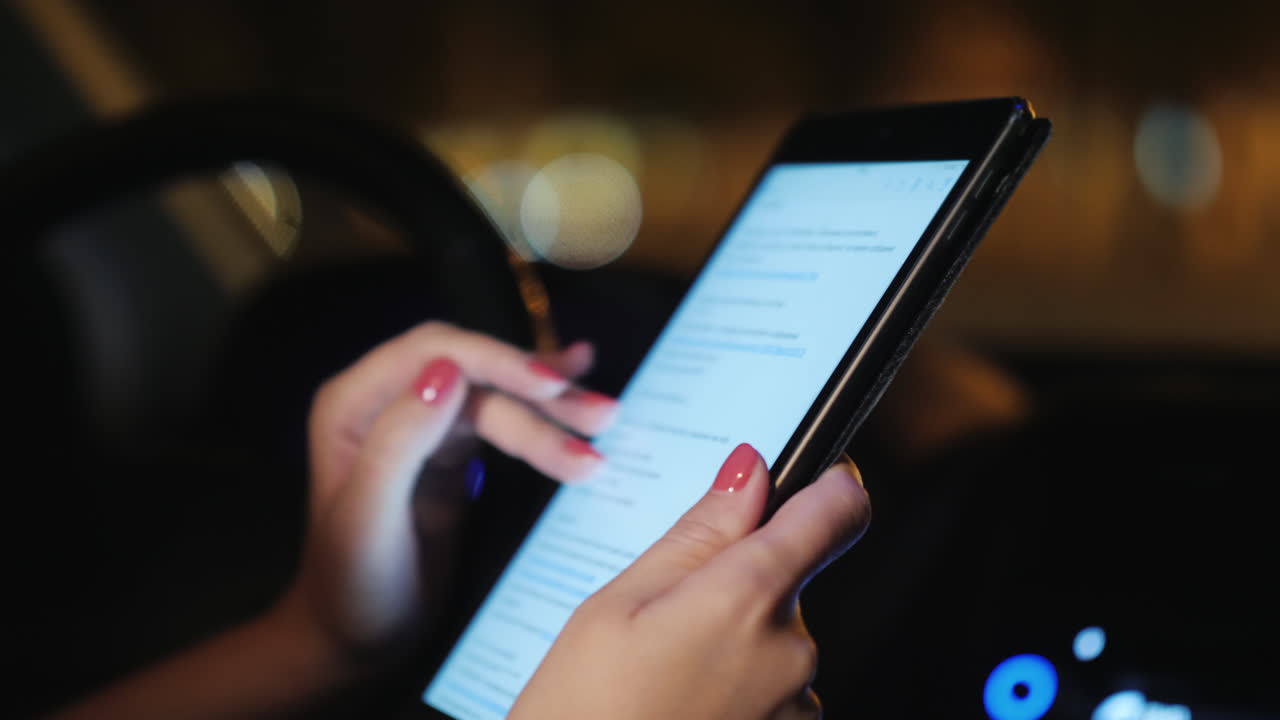 una mujer usa una tableta dentro del automóvil por la noche, el tráfico de automóviles es visible fuera del video de la ventana