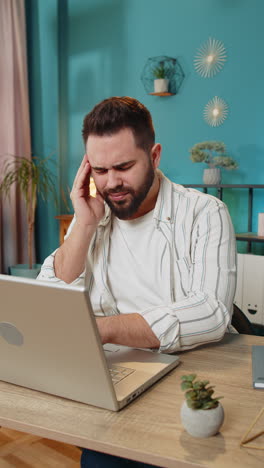 hombre con dolor de cabeza trabajando en una computadora portátil