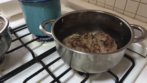 salt is added to beef steaks sizzling in steel pot on domestic gas stove
