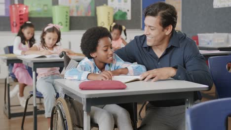 Feliz-Y-Diverso-Maestro-Hablando-Con-Un-Niño-En-Silla-De-Ruedas-En-Clase-De-Escuela-Primaria,-Cámara-Lenta