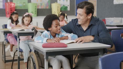 feliz y diverso maestro de sexo masculino hablando con un niño en silla de ruedas en clase de escuela primaria, cámara lenta