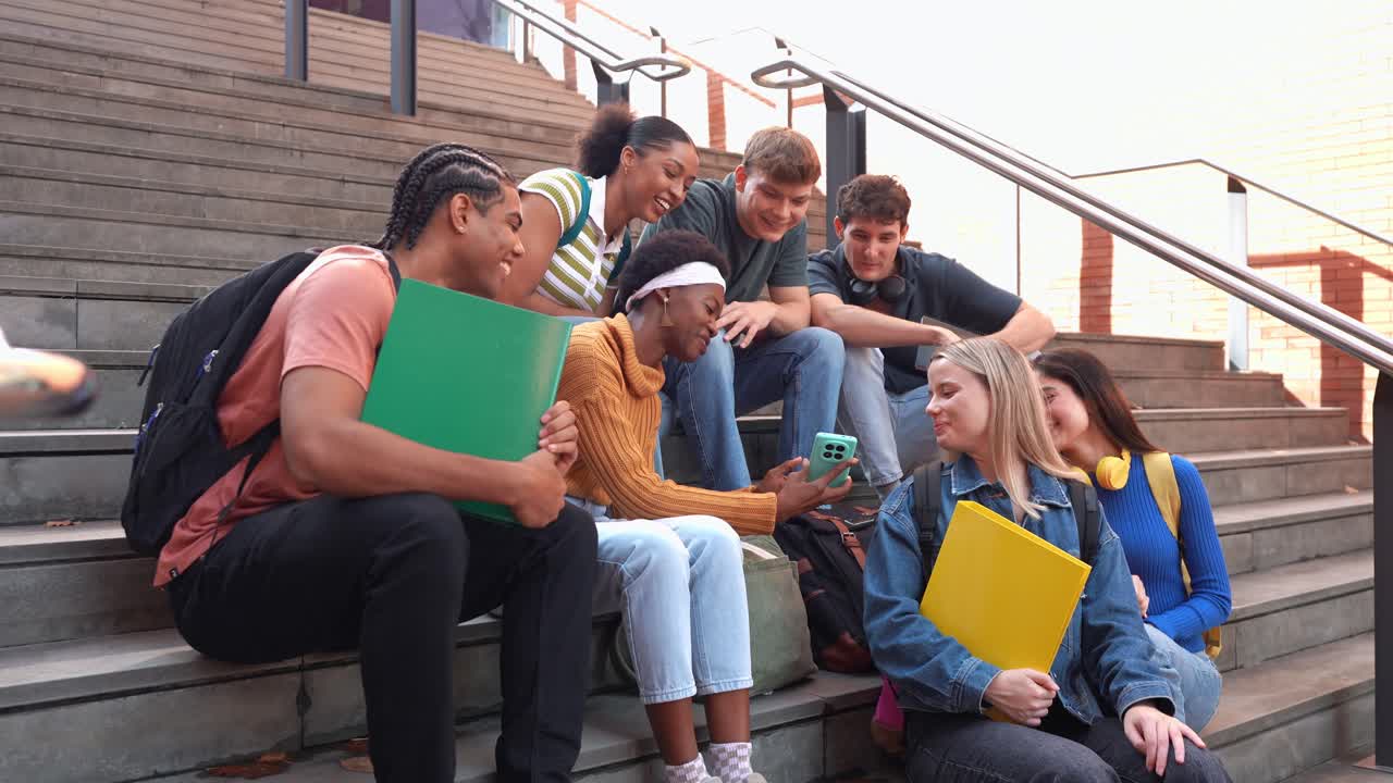En mangfoldig studentgruppe ler og bruker smarttelefon på campustrapper.