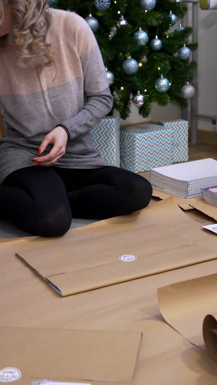 Woman Wrapping Christmas Gifts at Home With Decorated Christmas Tree, Vertical Shot