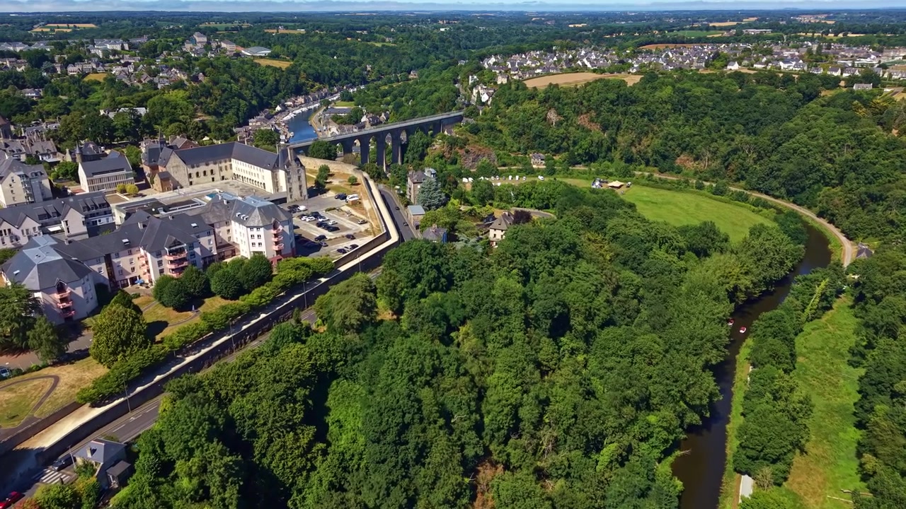 Floden La Rance strømmer gennem en frodig grøn dal med det historiske Dinan-viadukt i baggrunden i Bretagne, Frankrig. Luftfoto drone fremad.