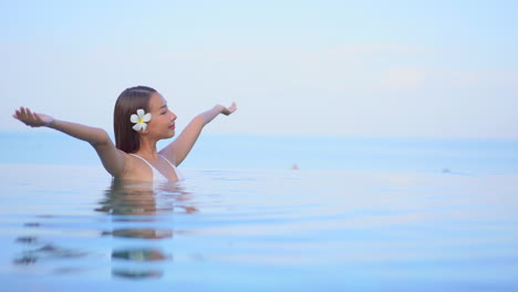 A-pretty-young-woman-in-chest-high-water-in-an-infinity-edge-pool-that-gives-the-illusion-of-a-continuous-waterscape