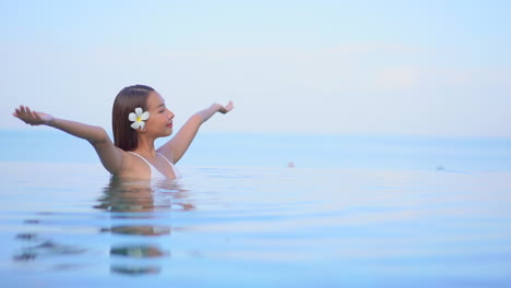 Eine-Hübsche-Junge-Frau-In-Brusthohem-Wasser-In-Einem-Infinity-Pool,-Der-Die-Illusion-Einer-Kontinuierlichen-Wasserlandschaft-Vermittelt