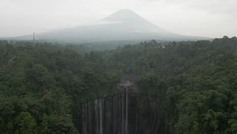 aerial: tumpak sewu waterfall in java jungle, volcano cone in distance