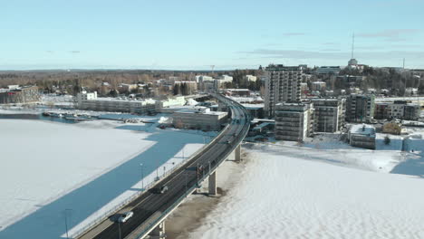 Antenne,-Tracking,-Drohnenaufnahme,-über-Pielisjoki-Und-Suvantosilta-Brücke,-Voller-Autos-Und-Verkehr,-Mit-Blick-Auf-Wohnhäuser-Und-Gebäude,-An-Einem-Sonnigen-Wintertag,-In-Joensuu,-Nordkarelien,-Finnland