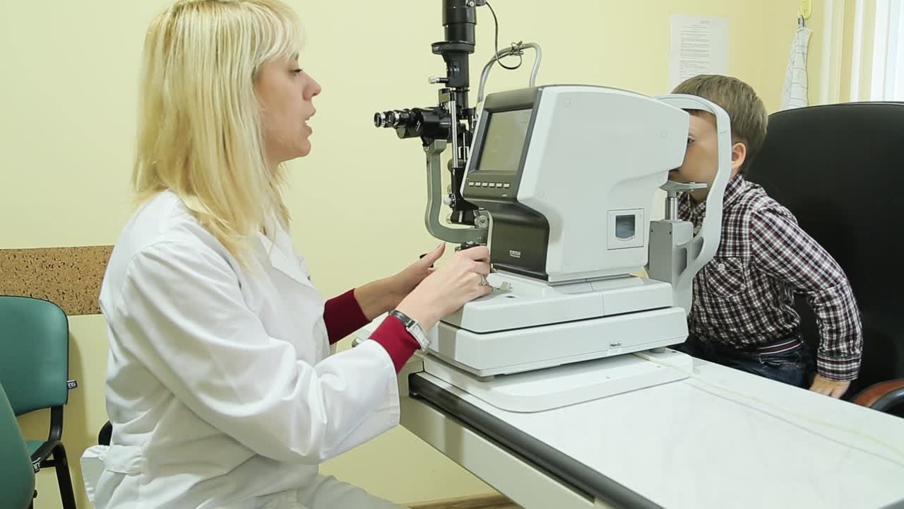 Female pediatric optician examining eyes of little boy with slit lamp device. Eye examination