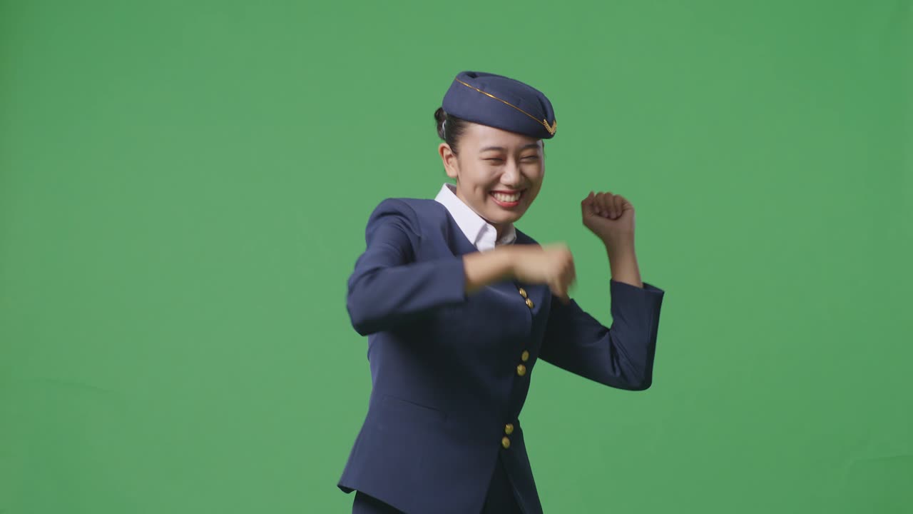 아시아 여성 승무원이 녹색 스크린 배경 스튜디오에 서서 춤을 추고 축하하고 있습니다.